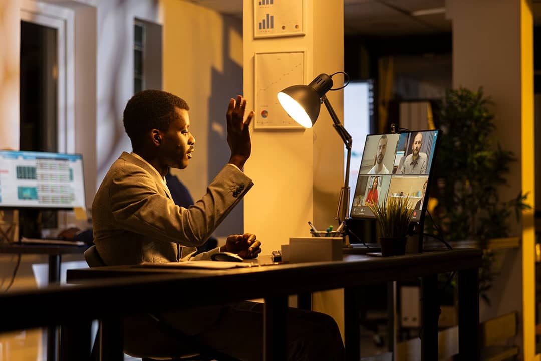 A professional interacting in an online conference with remote participants at his home office.